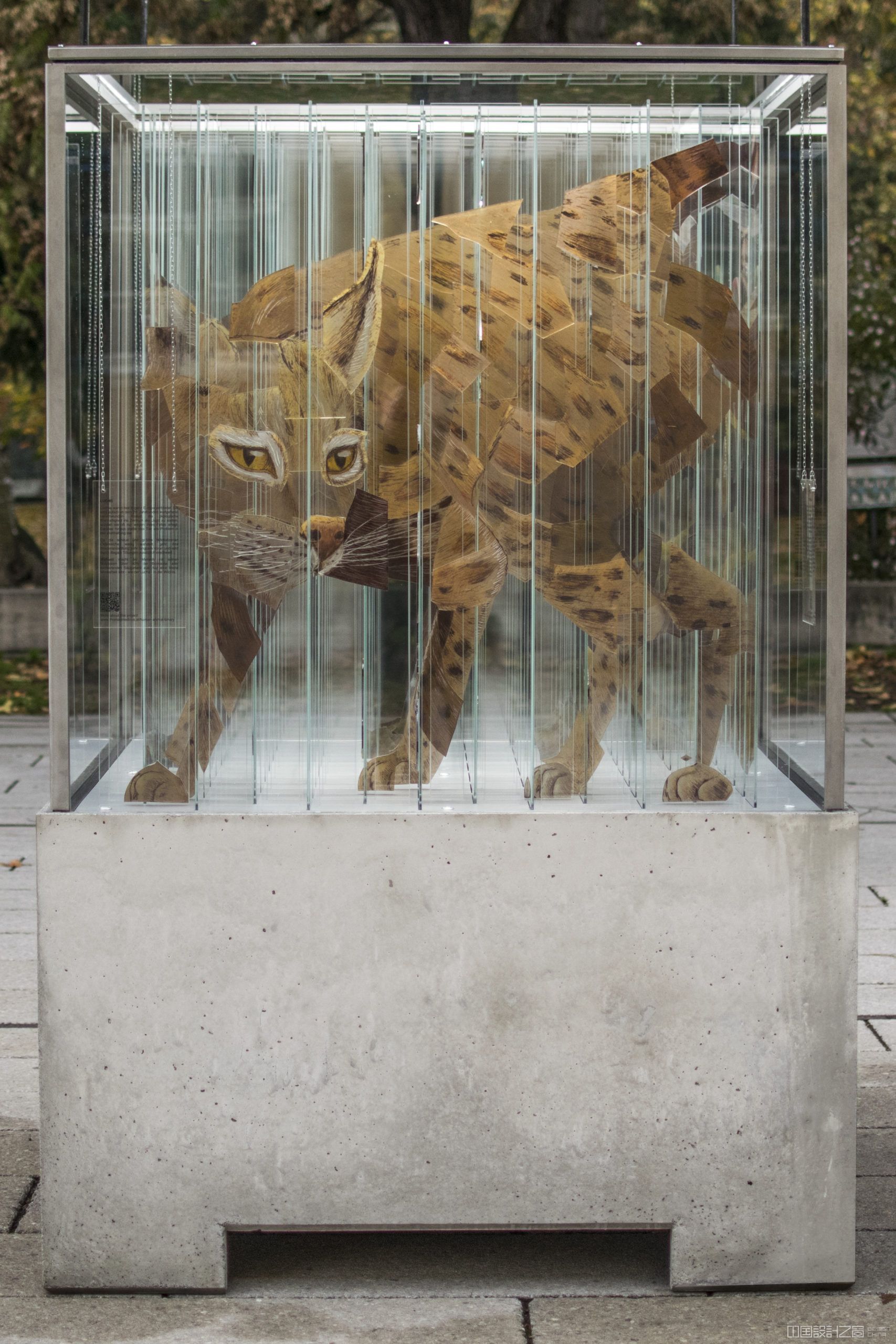 A sculpture in a glass and me<em></em>tal cube on a co<em></em>ncrete stand, co<em></em>ntaining more than 144 strips of glass that looks like a different animal on each side.