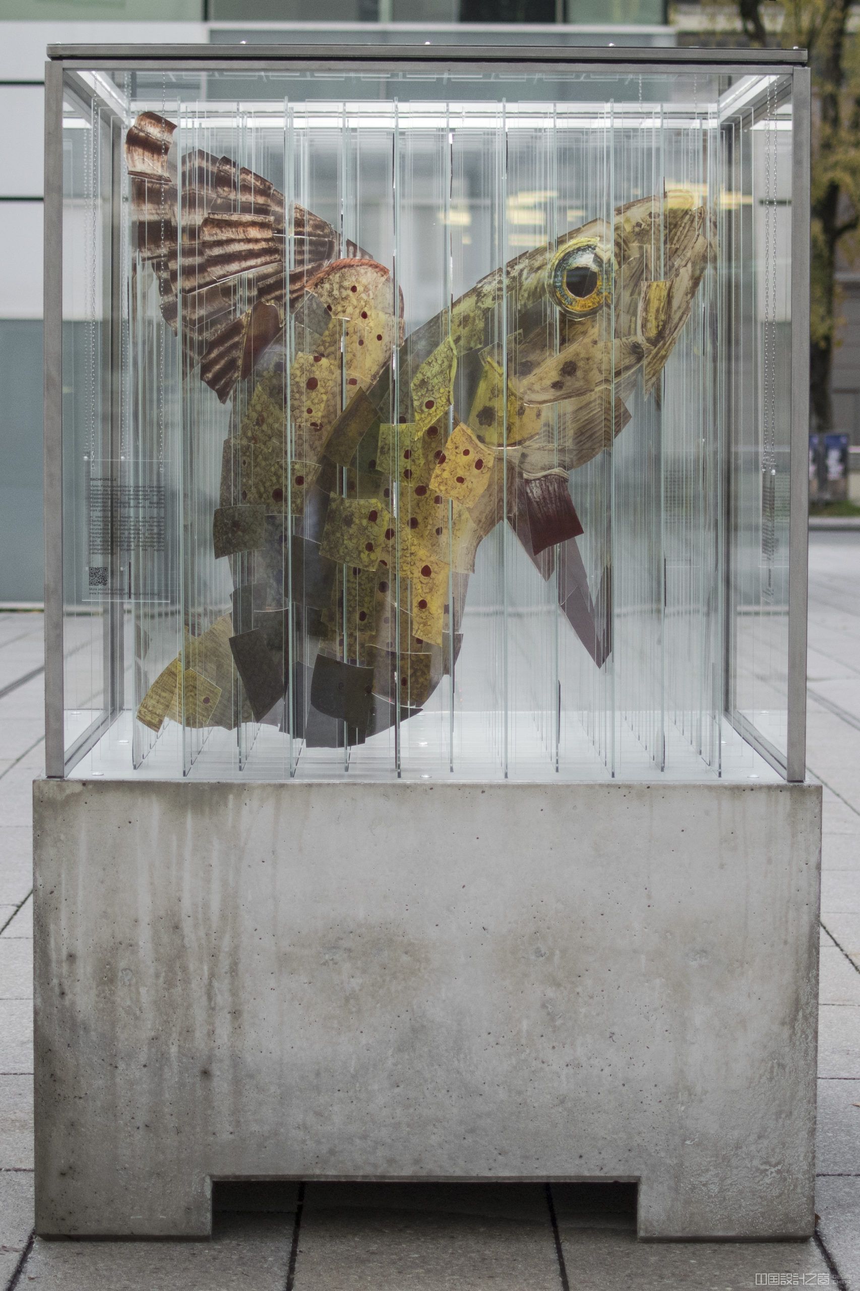 A sculpture in a glass and me<em></em>tal cube on a co<em></em>ncrete stand, co<em></em>ntaining more than 144 strips of glass that looks like a different animal on each side.