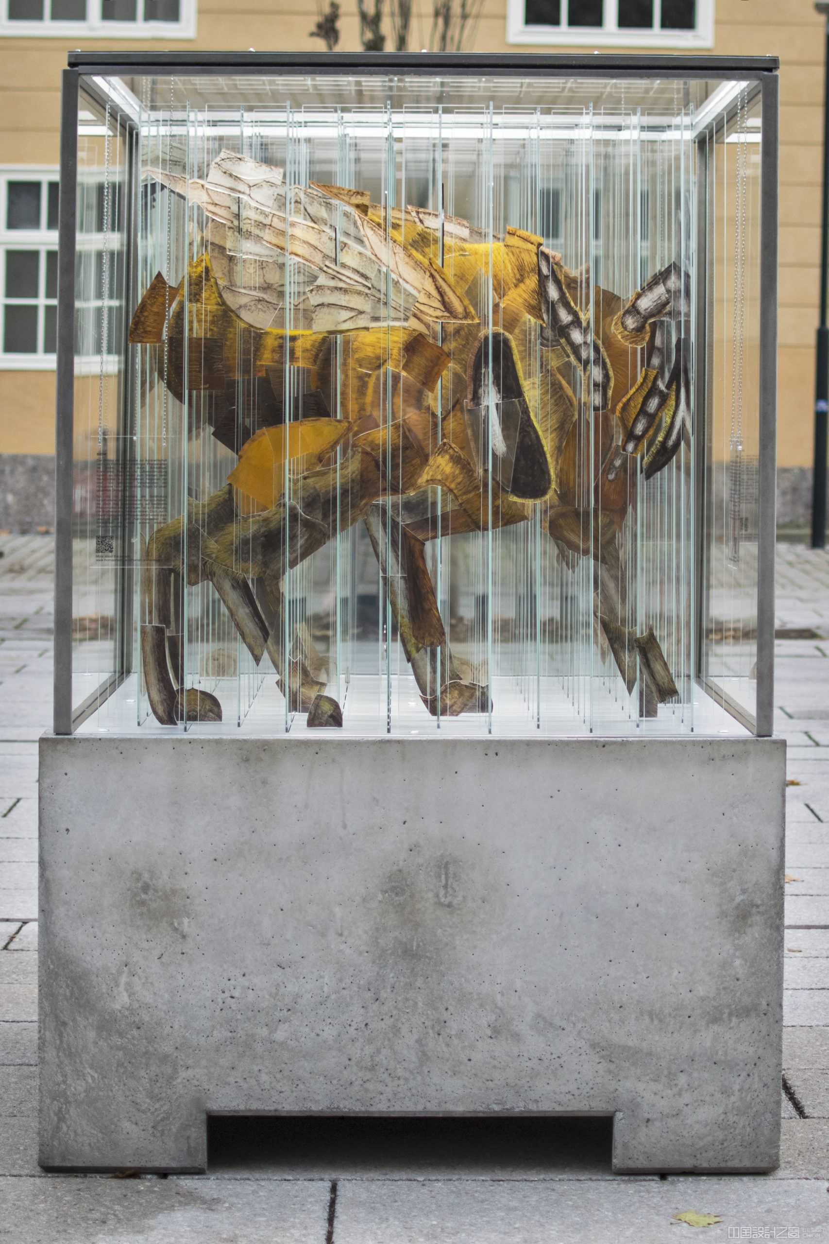 A sculpture in a glass and me<em></em>tal cube on a co<em></em>ncrete stand, co<em></em>ntaining more than 144 strips of glass that looks like a different animal on each side.