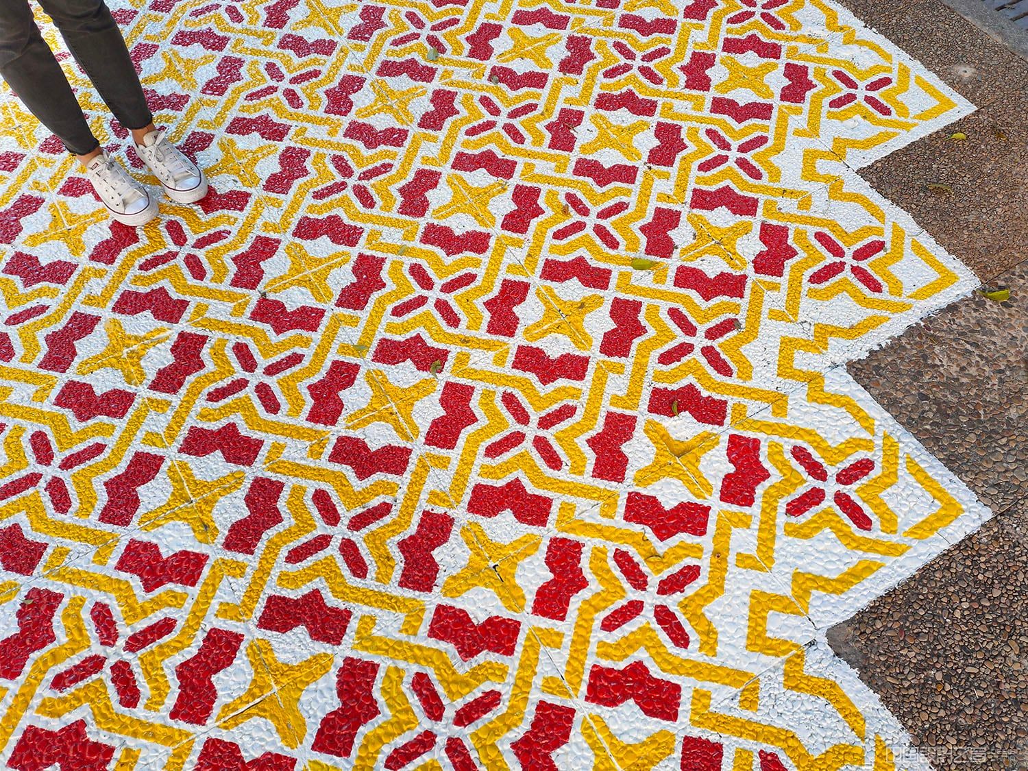 A detail photo of a vibrant patterned rug-like intervention painted on the co<em></em>ncrete in a city