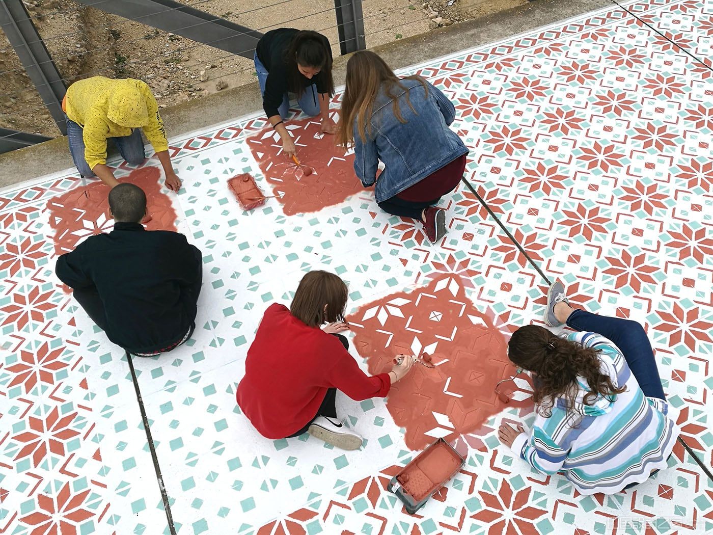 A photo of peopel painting a vibrant patterned rug-like intervention on the co<em></em>ncrete in a city