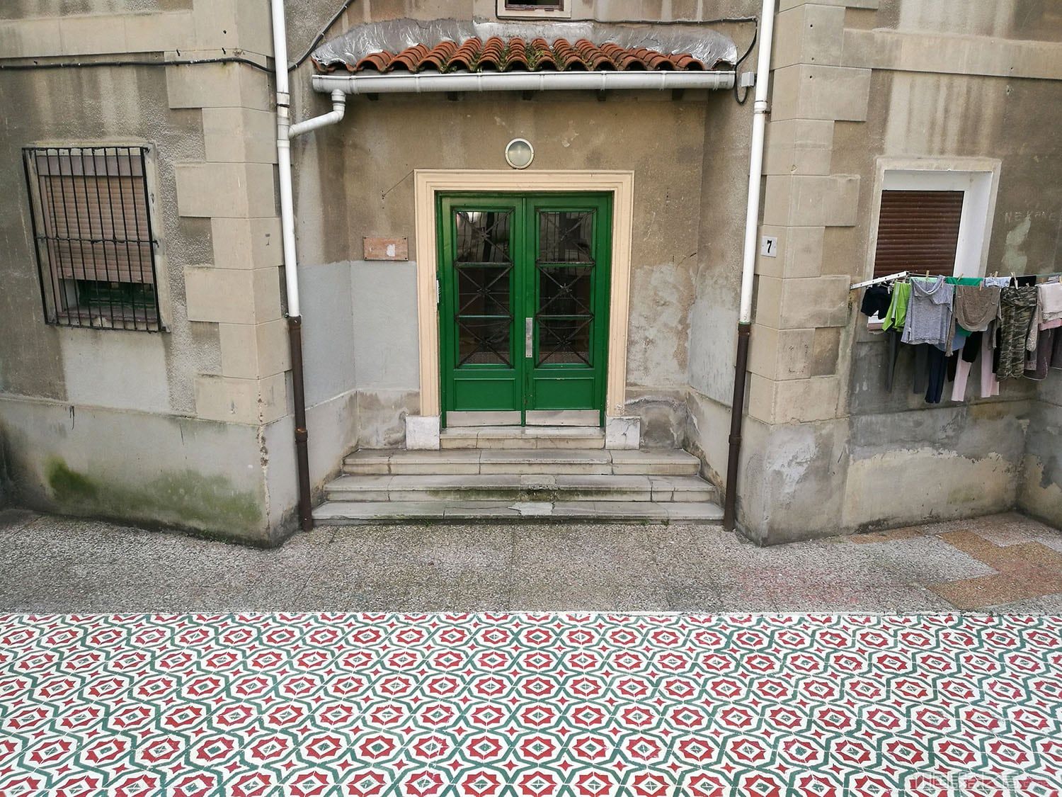 A photo of a vibrant patterned rug-like intervention painted on the co<em></em>ncrete in a city