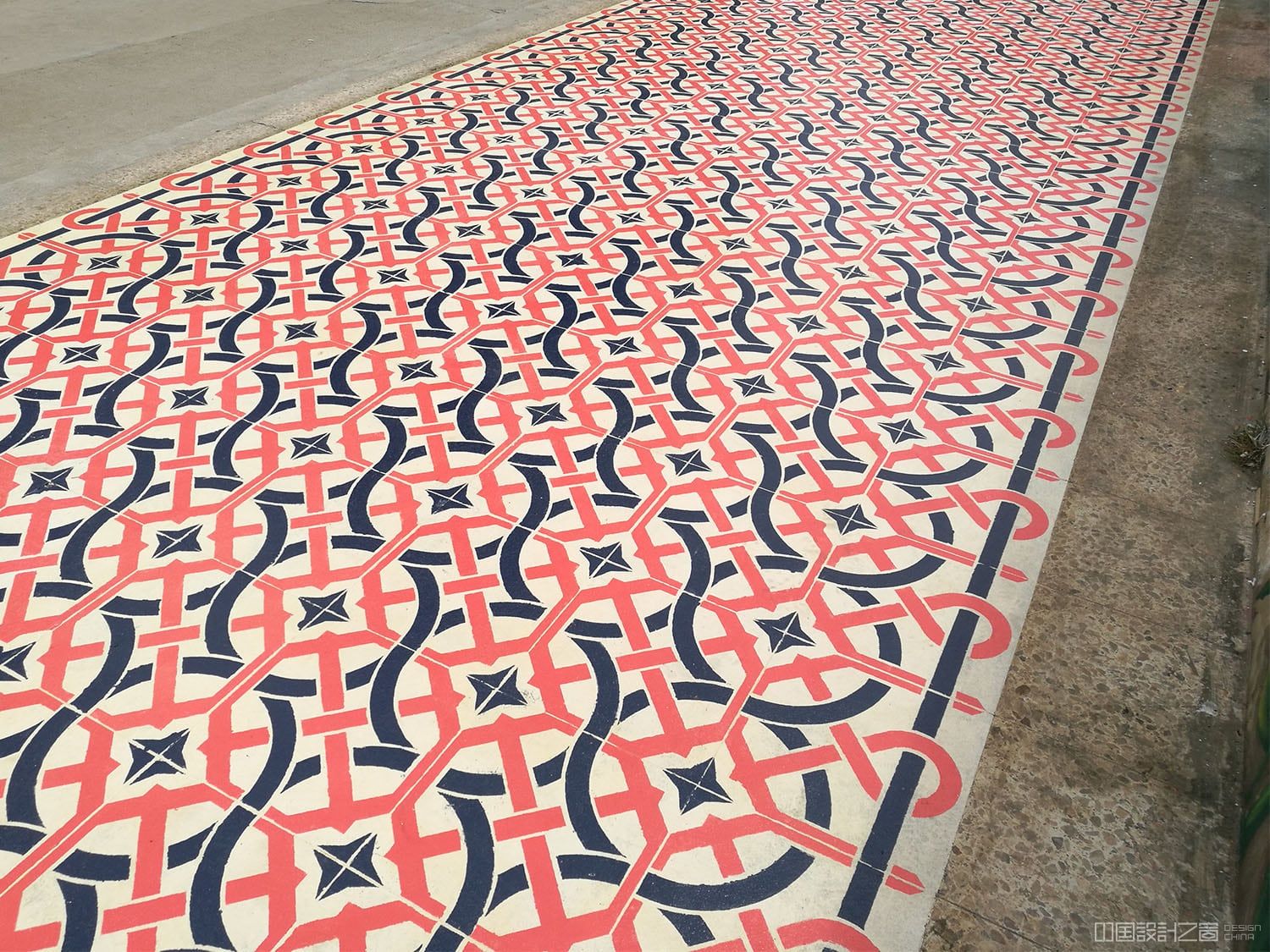 A photo of a vibrant patterned rug-like intervention painted on the co<em></em>ncrete in a city