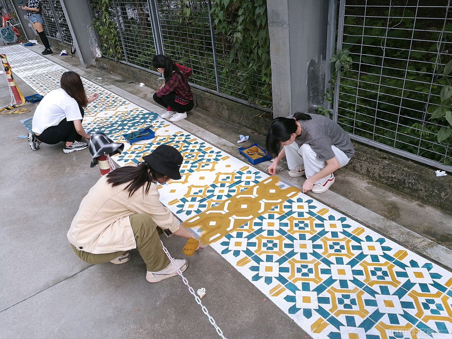 A photo of people painting a vibrant patterned rug-like intervention on the co<em></em>ncrete in a city
